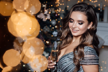 Obraz na płótnie Canvas Party, drinks, holidays, luxury and celebration concept - smiling woman in evening dress with glass of champagne over Christmas background. Winter holiday. Lights around.