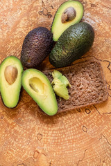 Slices of avocado and whole avocado fruit with rye bread on a wooden background.