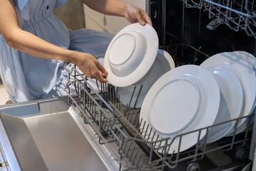 Woman hand putting a plate in the dishwasher.