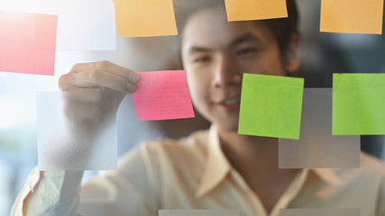 Photo of young businessman while sticky post it on glass. Meeting and sharing idea concept. Reminder schedule board.