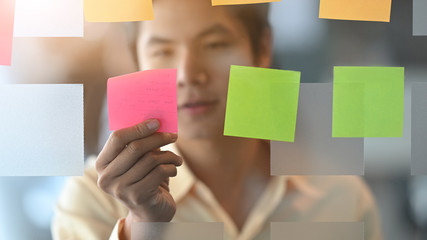 Photo of young businessman while sticky post it on glass. Meeting and sharing idea concept. Reminder schedule board.