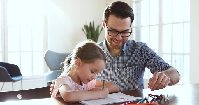 Happy dad teaching little cute girl drawing with colored pencils