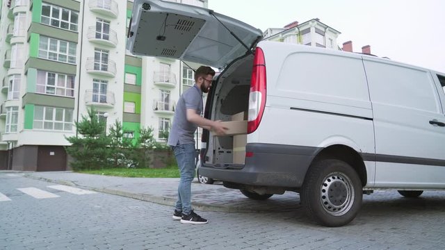 Bearded courier unloading cardboard boxes from car trunk