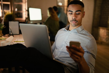 African American businessman texting on mobile phone while working late on a computer.