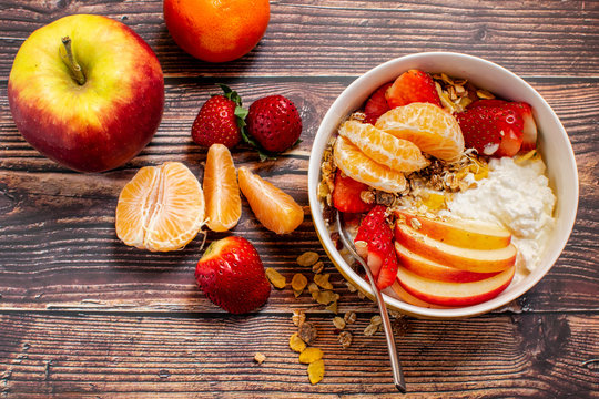 A Bowl Of Muesli And Cottage Cheese. With Slices Of Strawberries, Apple And Tangerines. Rustic Brown Wooden Surface. Flat Lay.