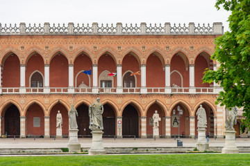 Loggia Amulea in red brick and terracotta neo-Gothic style building, with double loggia facing Prato della Valle, Padua, Italy, 1860. View with statues in the square.