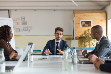 Focused project manager communicating with workers. Thoughtful employees sitting at table during morning briefing. Business meeting concept
