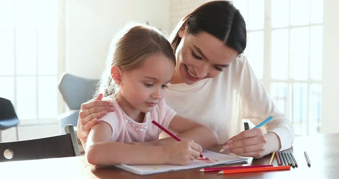 Caring mom embrace help kid daughter drawing picture with pencils