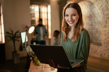 Portrait of happy businesswoman working late on laptop in the office.