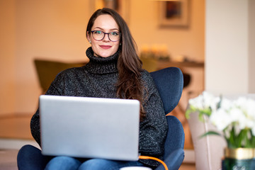 Shot of young woman with her notebook sitting on chair while working from home