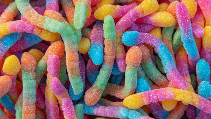 Pile of neon sugary gummy worms or  chewy sour crawlers background. Close-up of colorful and flavorsome sweet and sour treats coated in sugar crystals for bulk or individual sale at a candy store.