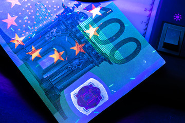 100 Euro banknote. Lying in the ultraviolet to verify the authenticity of banknotes. Close-up