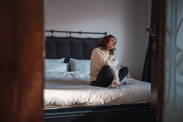 Obraz premium Young woman sitting in bed relaxed, smiling and enjoying the morning