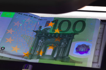 100 Euro banknote. Lying in the ultraviolet to verify the authenticity of banknotes. Close-up