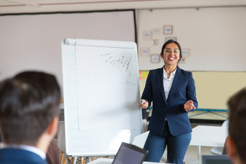 Smiling Asian business consultant working with employees. Beautiful young businesswoman standing near whiteboard and explaining new information. Business training concept