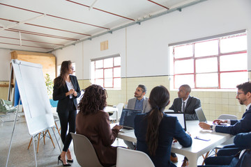 Confident female business trainer working with employees. Group of workers sitting at table and...