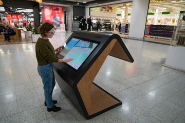 Woman with phone uses self-service kiosk in the shopping mall