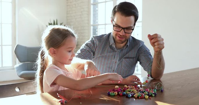 Caring father helping little child daughter stringing necklace of beads