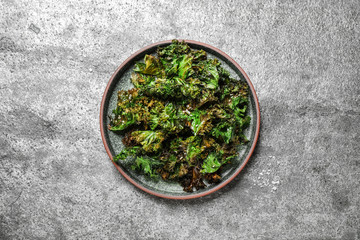 Tasty baked kale chips on grey table, top view