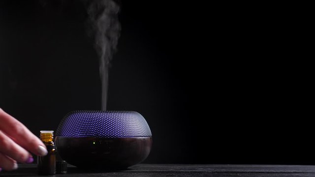 Woman add essential oil into Diffuser on black wooden table, closeup