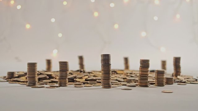 The concept of money. Columns of gold coins in the form of skyscrapers or Stonehenge. Close-up hands make up stacks of coins. Smoke. Garland.