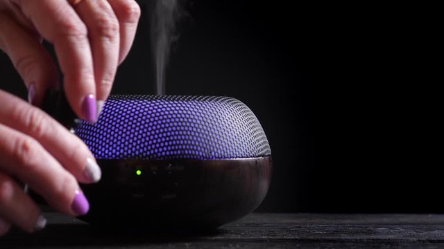 Woman add essential oil into Diffuser on black wooden table, closeup