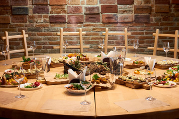Wooden table with a set of variety snacks, different vegetable salads, salad, pickle carrot, kavarma, rye bread sandwiches with soft cheese cream against a brick wall