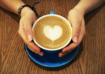 Cup of latte coffee with heart symbol on wooden background