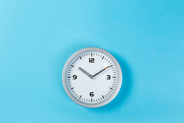 Fototapeta na wymiar White wall clock with a yellow used hanging on the wall. Minimalist image of a wall clock on a blue background with copy space