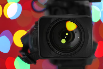 Modern video camera against blurred colorful lights, closeup
