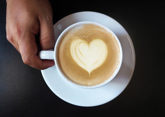 Cup of latte coffee with heart symbol on black background