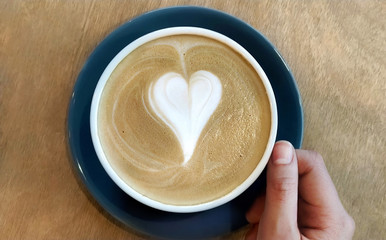 Cup of latte coffee with heart symbol on wooden background