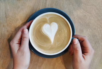 Cup of latte coffee with heart symbol on wooden background