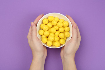 Woman holding bowl of lemon drops on purple background, top view