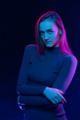Young beautiful model in sweater in colored light, colored neon lamps blue and purple.