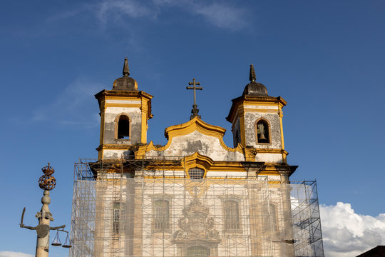 Pillory with justice balance and sword on the main square in Mariana, Minas Gerais, Brazil, with church in scaffolding behind against a blue sky