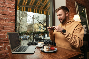 Male blogger taking photo of dessert and coffee at table in cafe