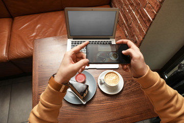 Male blogger taking photo of dessert and coffee at table in cafe, closeup
