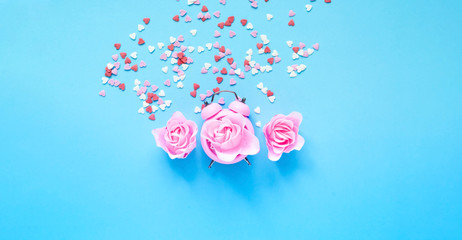 Festive concept with alarm clock and roses flower on blue background. Valentines Day. Close-up, copy space