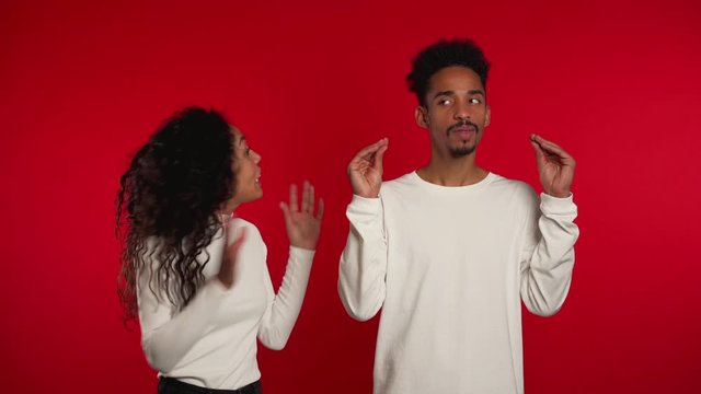 African man showing bla-bla-bla gesture with hands and rolling eyes while girlfriend trying to say something. Couple isolated on red background. Empty promises, blah concept. Lier.