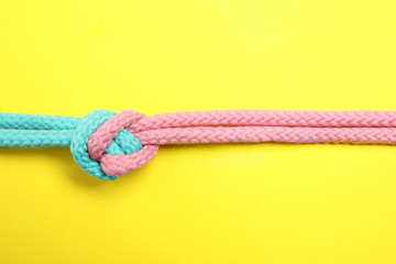 Colorful ropes tied together on yellow background, top view. Unity concept - obrazy, fototapety, plakaty