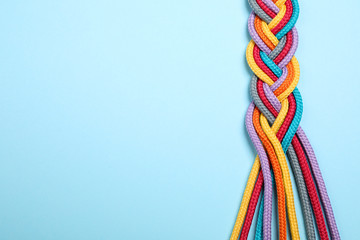 Top view of braided colorful ropes on light blue background, space for text. Unity concept - obrazy, fototapety, plakaty