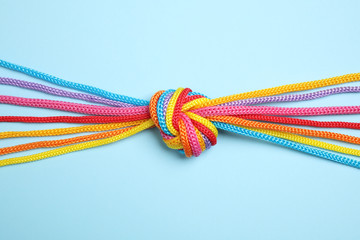 Colorful ropes tied together on light blue background, top view. Unity concept