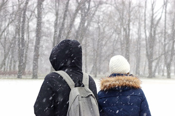 young couple standing in a park while snow falls down © schapinskaja