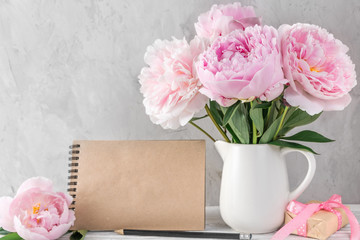 Still life with pink pastel peony flowers, gift box and blank paper card on white table. mock up