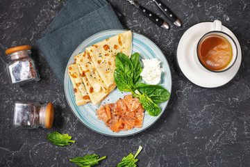 Delicious breakfast or brunch - crepes with smoked salmon, spinach and sour cream on stone background.