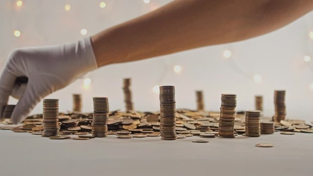 The concept of money. Columns of gold coins in the form of skyscrapers or Stonehenge. Close-up hands make up stacks of coins. Smoke. Garland.