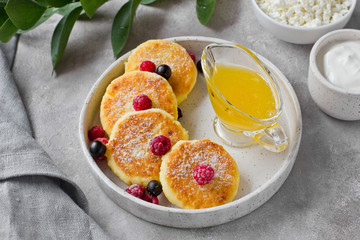 Cottage cheese pancakes or syrniki with honey, raspberry, blackcurrant and sour cream on hand-made ceramic plate