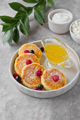Cottage cheese pancakes or syrniki with honey, raspberry, blackcurrant and sour cream on hand-made ceramic plate