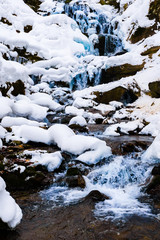 Mountain waterfall rolling down in winter, close up. Frost and icicles concept